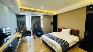 A hotel room with a bed, a desk, a chair, a TV, and a window with curtains.