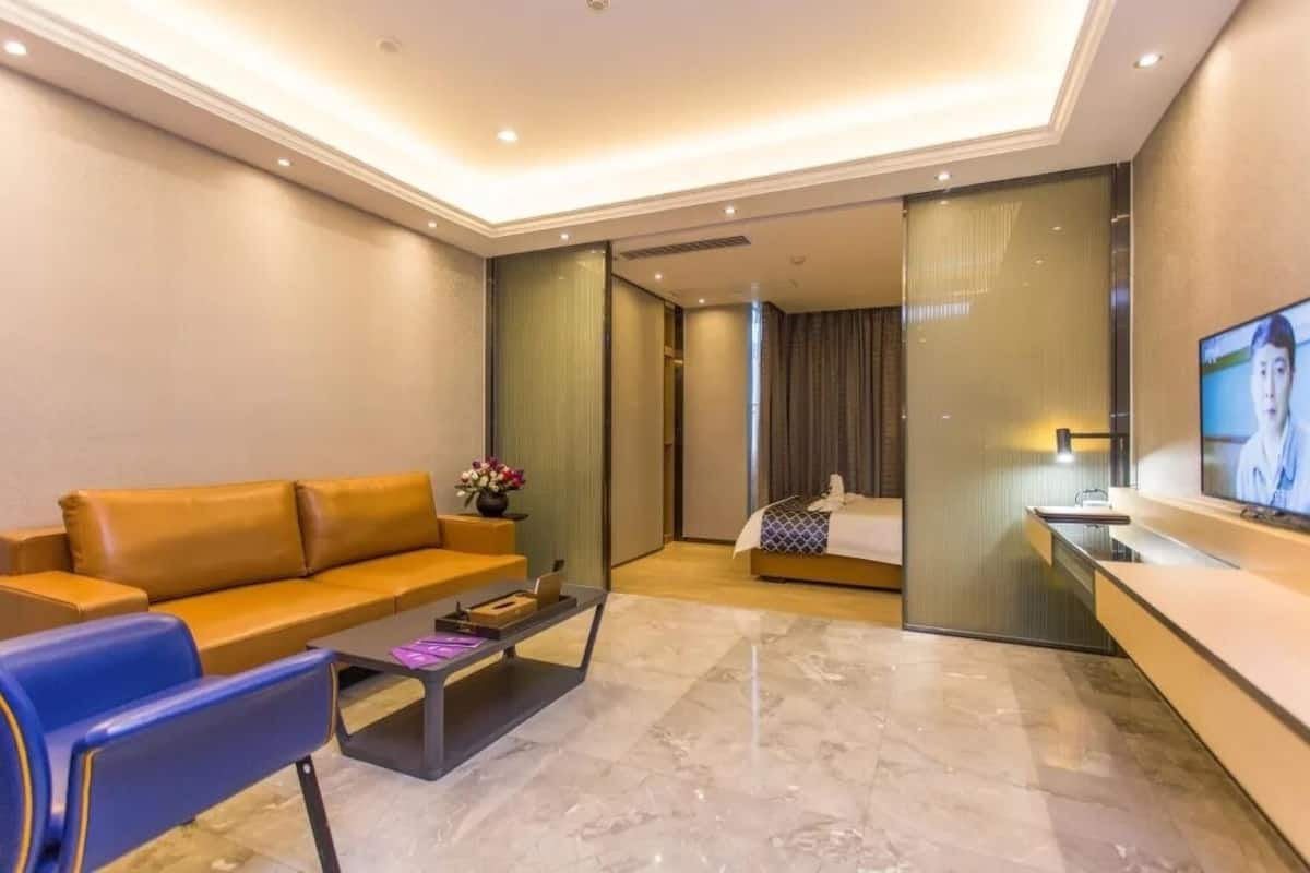 A modern hotel room with a sofa, a coffee table, a TV, and a sliding door leading to a bedroom.