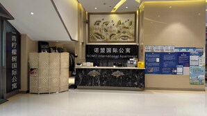 A reception desk with a sign for NIMO international apartment, a wall with informational posters, and a decorative wall piece above the desk. - Green Lemon Tree International Apartment - Beijing Road Jiedeng Metropolis Branch (Guangzhou)
