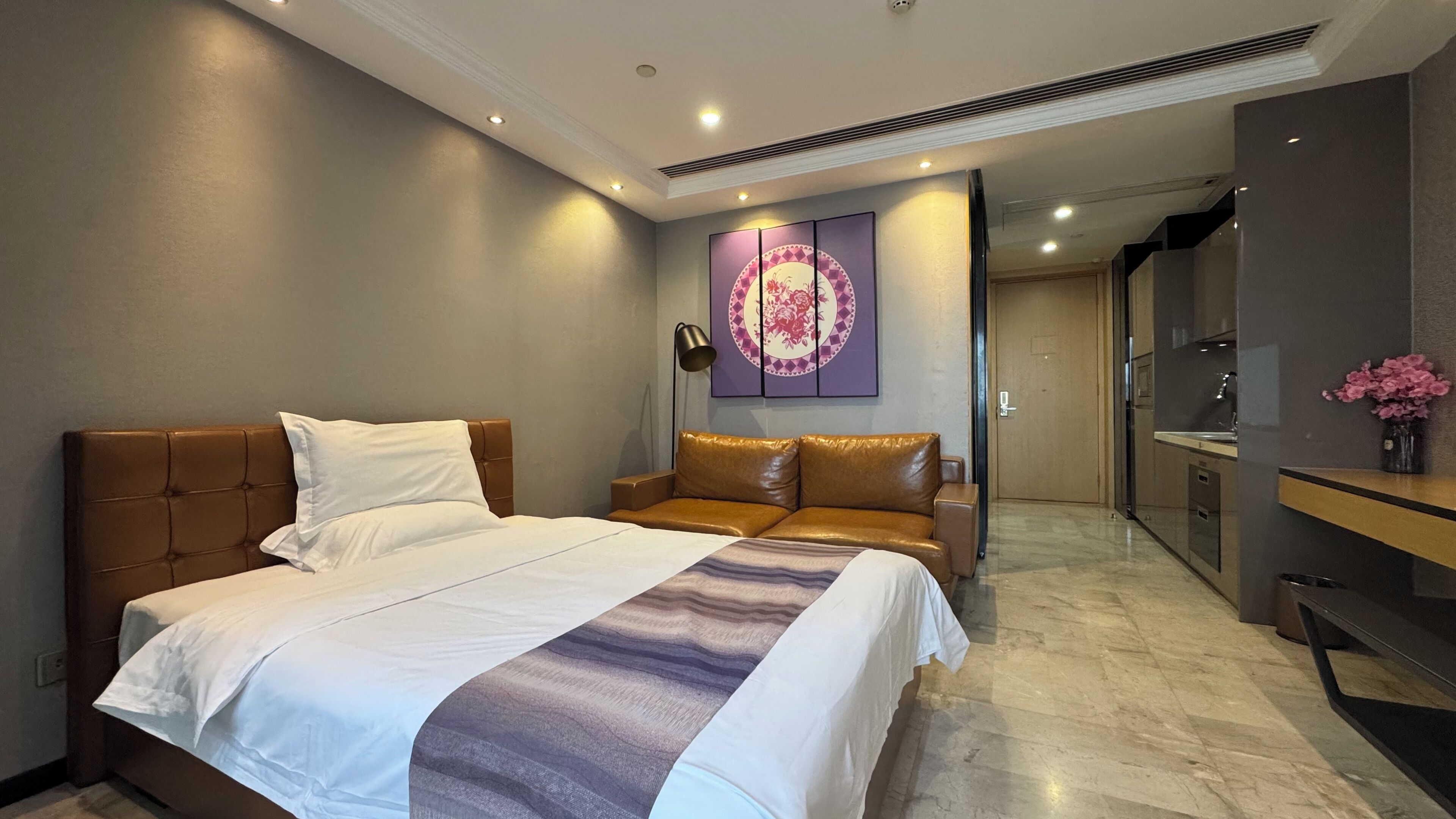 A modern hotel room with a large bed, a sofa, a desk, and a bathroom visible through an open door.
