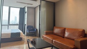 A modern hotel room with a large bed, a leather sofa, a small table, and a chair. - Green Lemon Tree International Apartment - Beijing Road Jiedeng Metropolis Branch (Guangzhou)