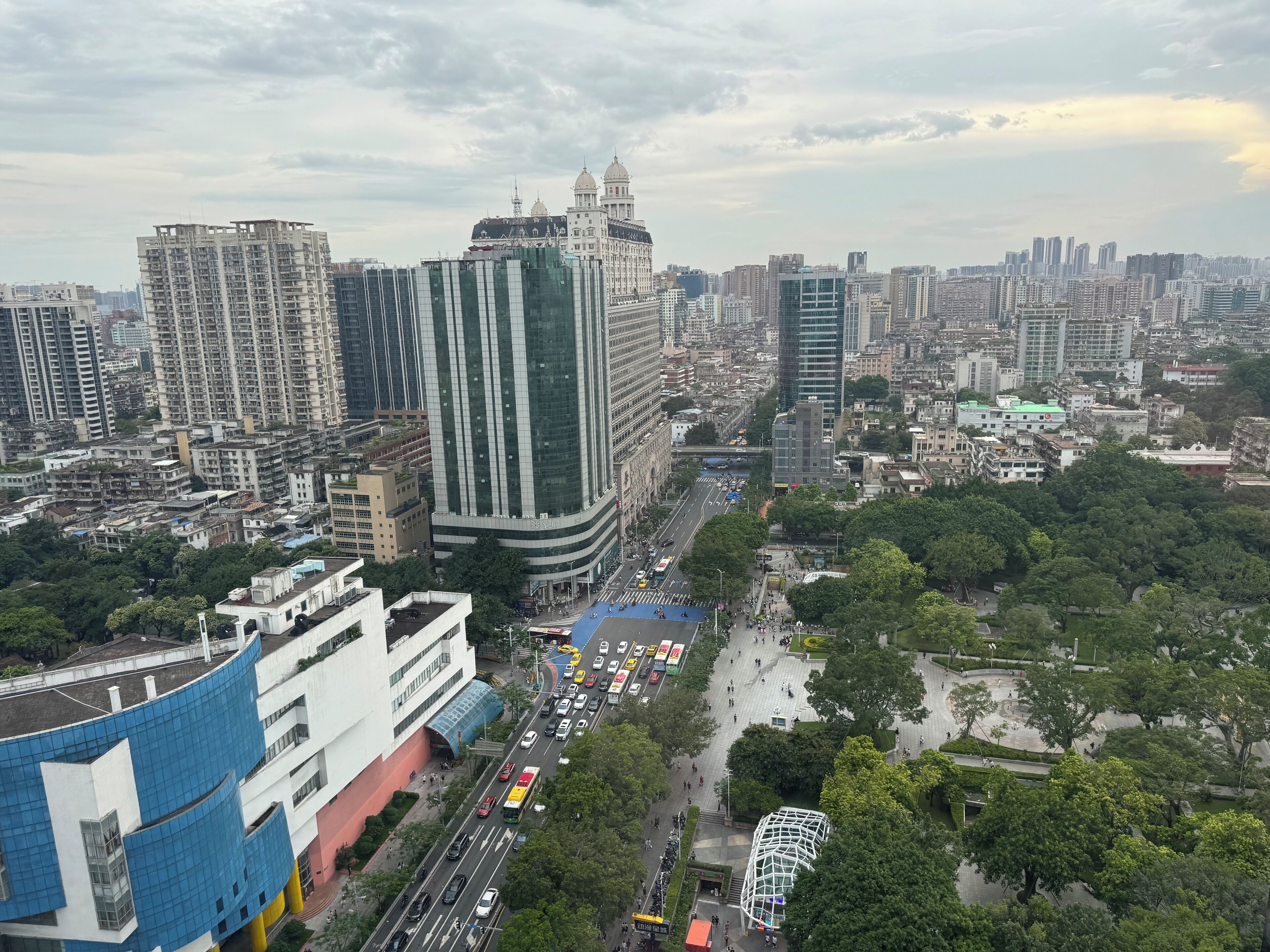A cityscape with high-rise buildings, a curved modern building with a blue roof, and a busy street with vehicles and pedestrians.