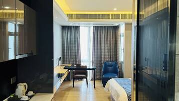 A modern hotel room with a kitchenette, a dining area, a bed, and a view of the outdoors.