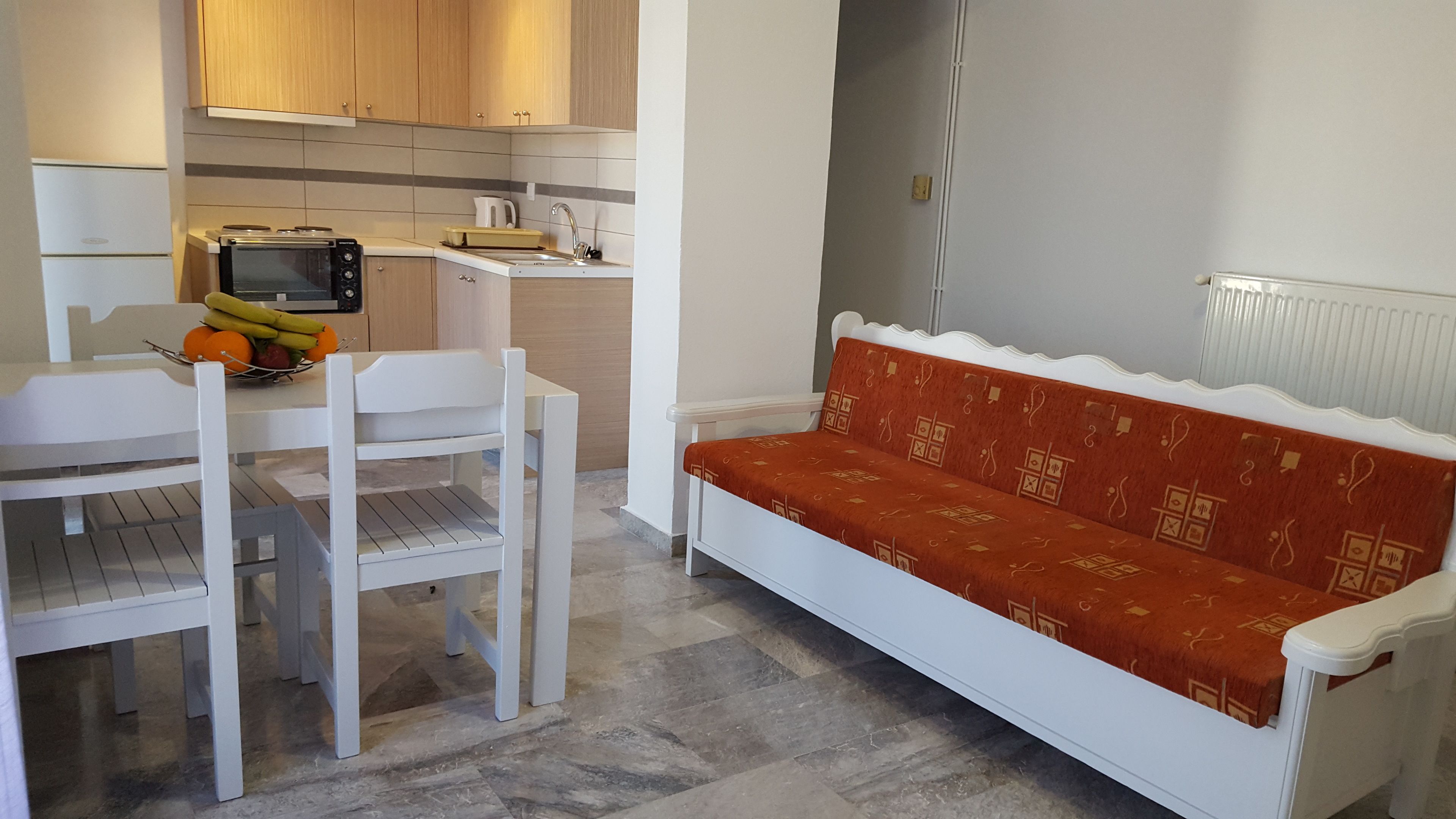 Une cuisine compacte avec des meubles blancs, un four encastré et un coin repas comprenant une table et des chaises blanches.