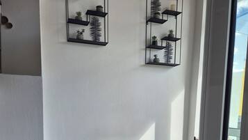 A modern interior with a tiled floor, a large potted plant, and two wall-mounted shelves with decorative items.