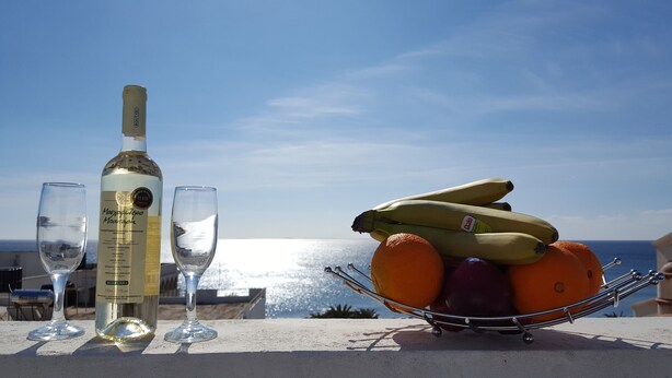 A bottle of wine, two glasses, and a fruit bowl with bananas and oranges on a balcony overlooking the sea. - Varmy (Ierapetra)