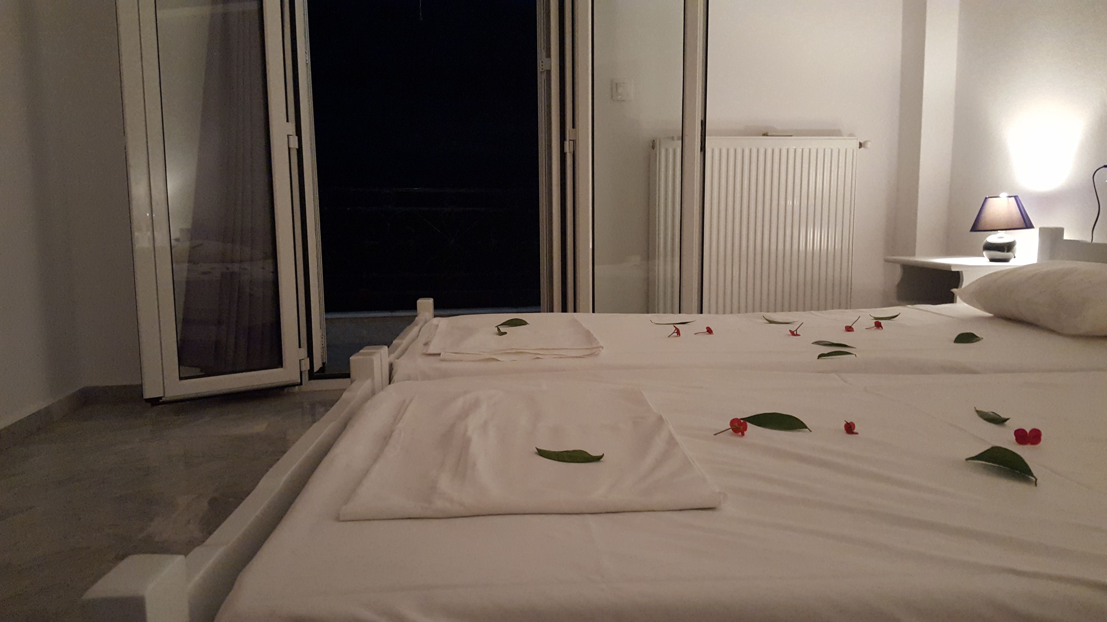 A hotel room with a bed, a nightstand, a lamp, and a window with blinds.