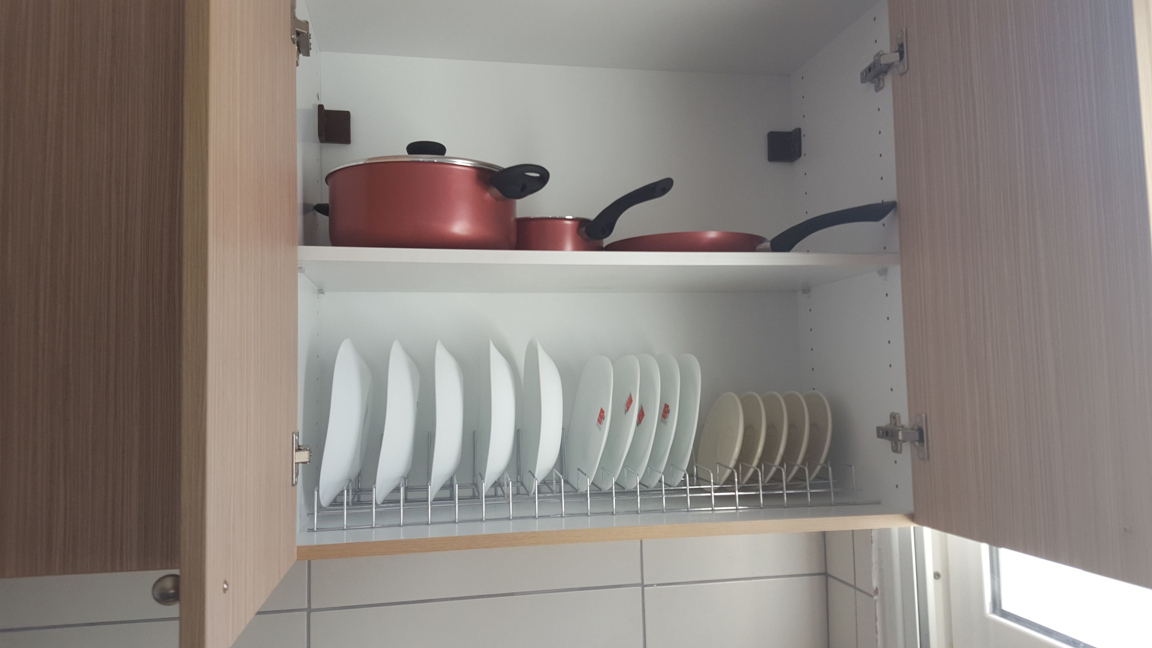 Una cucina con mobili in legno, un espositore per piatti bianchi e pentole rosse sullo scaffale superiore.