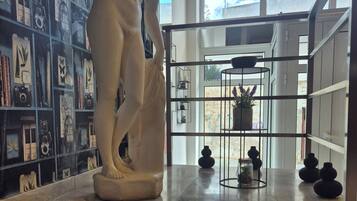 A marble floor with a white statue, a wall with framed pictures, and a view of the sky through a window.