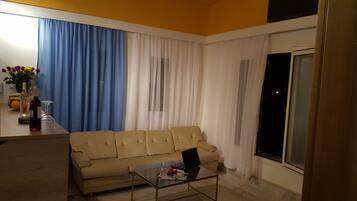 Una sala de estar con un sofá color beige, una mesa de centro con una computadora portátil y una ventana con cortinas.