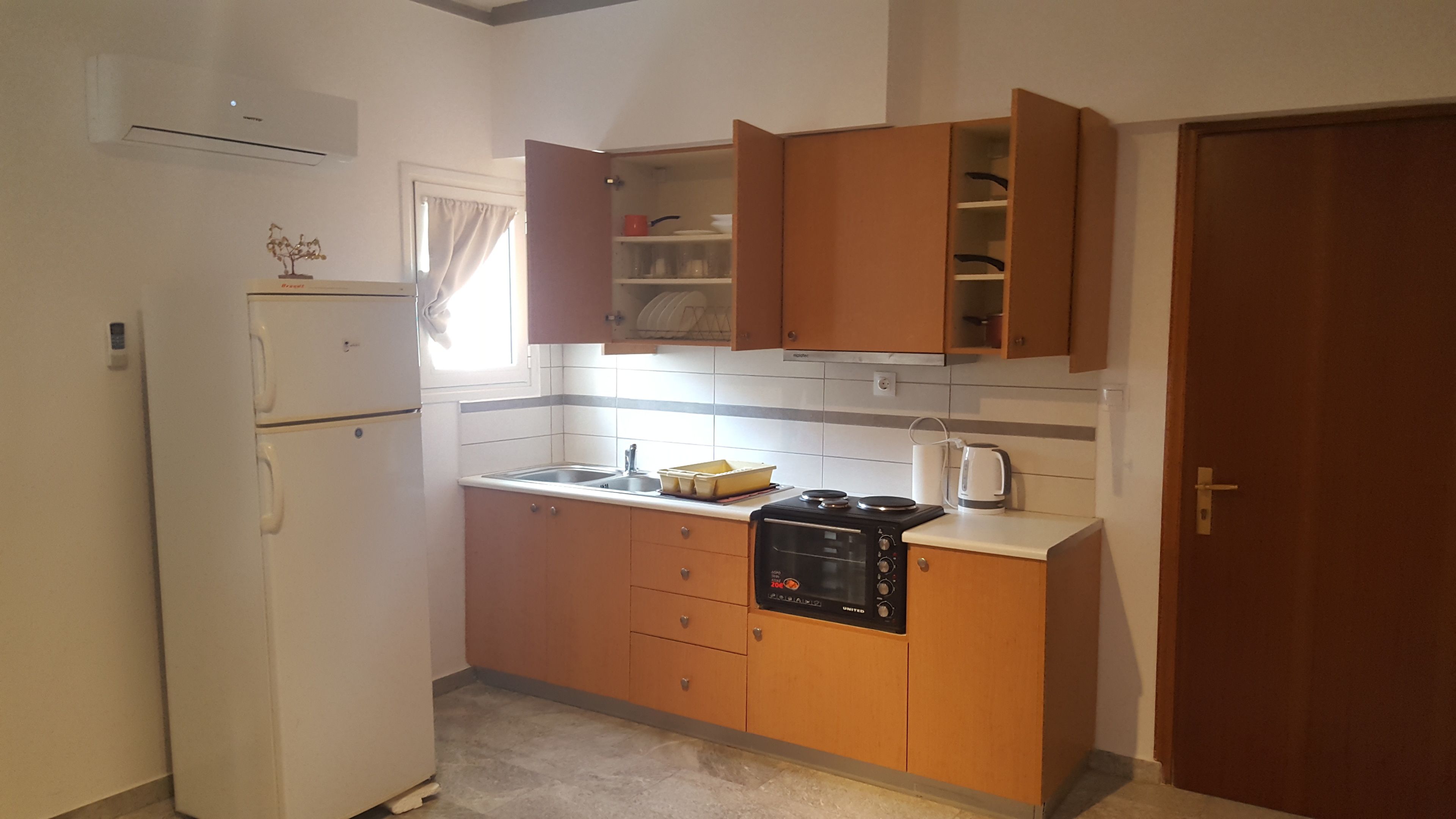 A compact kitchen with a white refrigerator, wooden cabinets, a built-in oven, and a window with curtains.