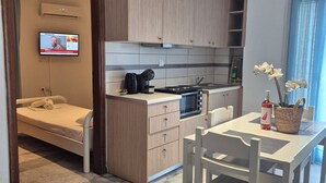 A modern kitchen with wooden cabinets, a built-in microwave, and a dining area with a table and chairs. - Varmy (Ierapetra)
