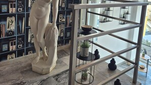A statue in a room with a blue bookshelf filled with various items. - Varmy (Ierapetra)