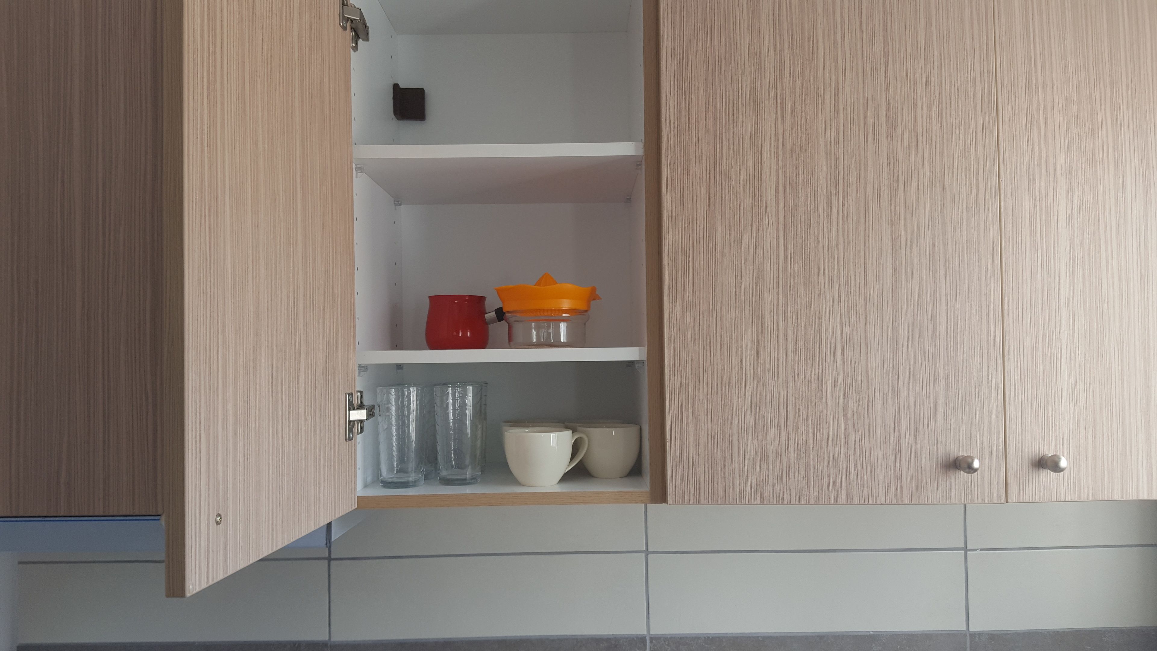 A kitchen with wooden cabinets, a white shelf, and a tiled backsplash.