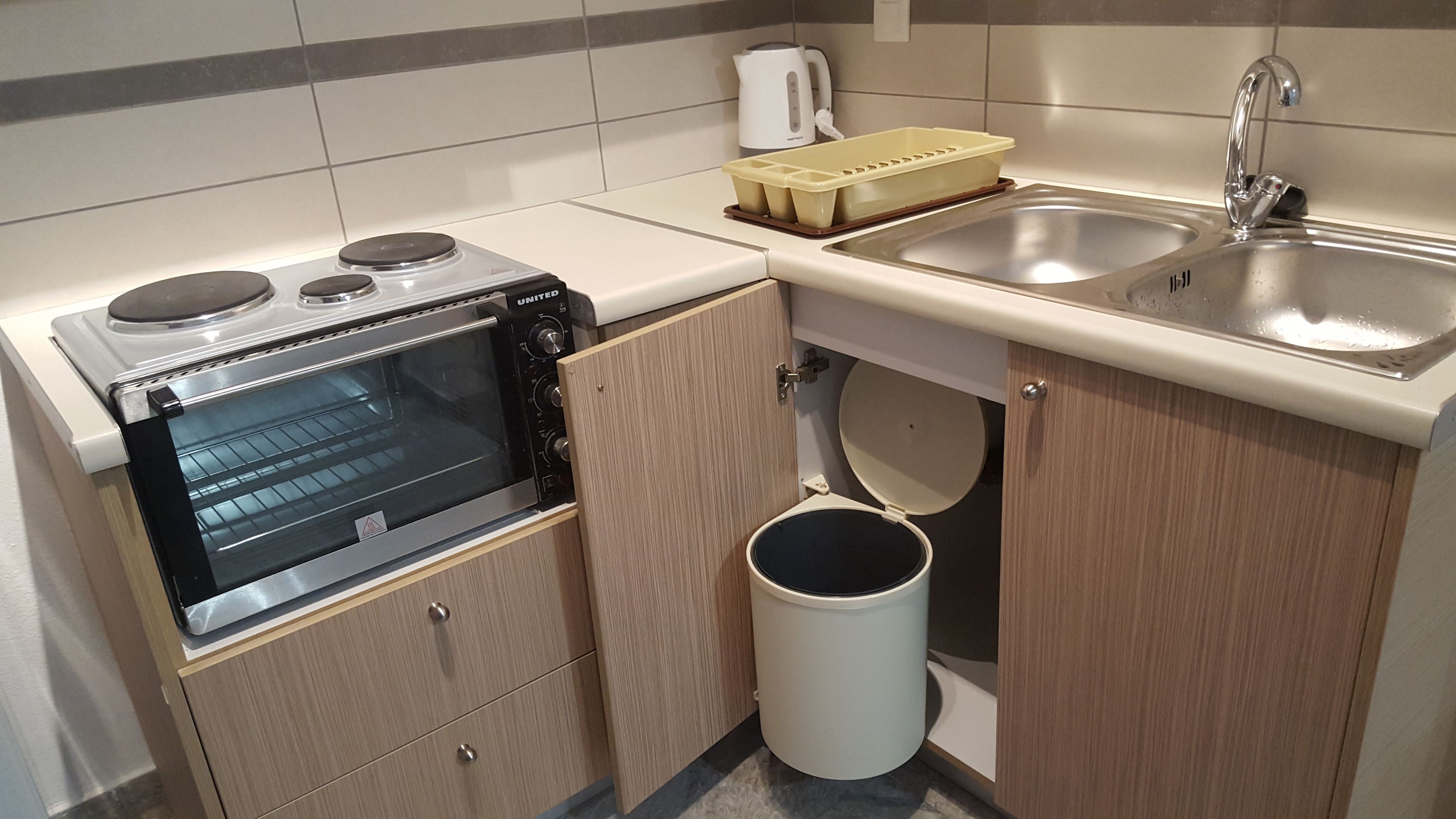 A compact kitchen with a built-in oven, a sink, and a trash bin.