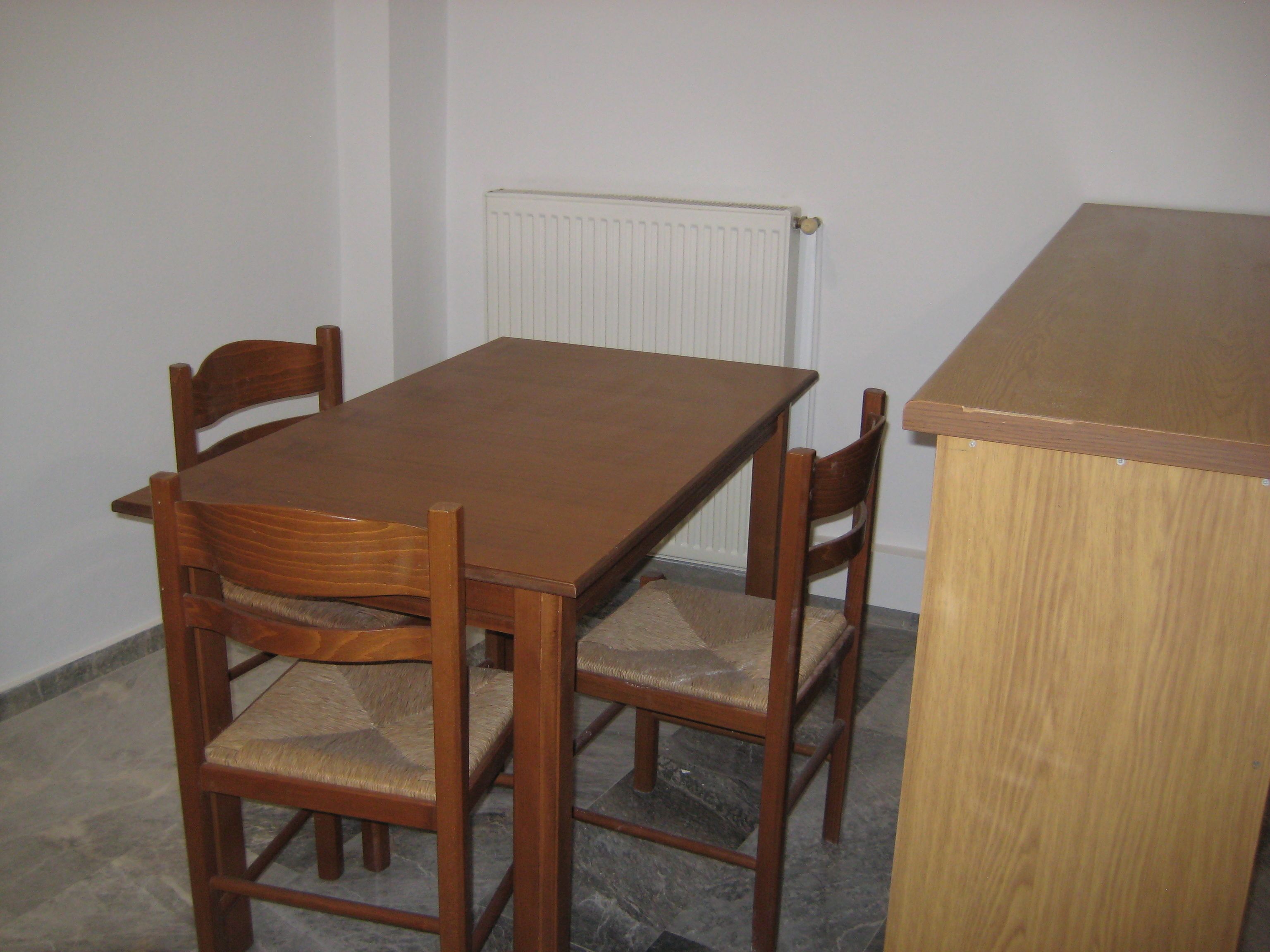 Una mesa de madera con cuatro sillas, un radiador y un pequeño mostrador de madera.