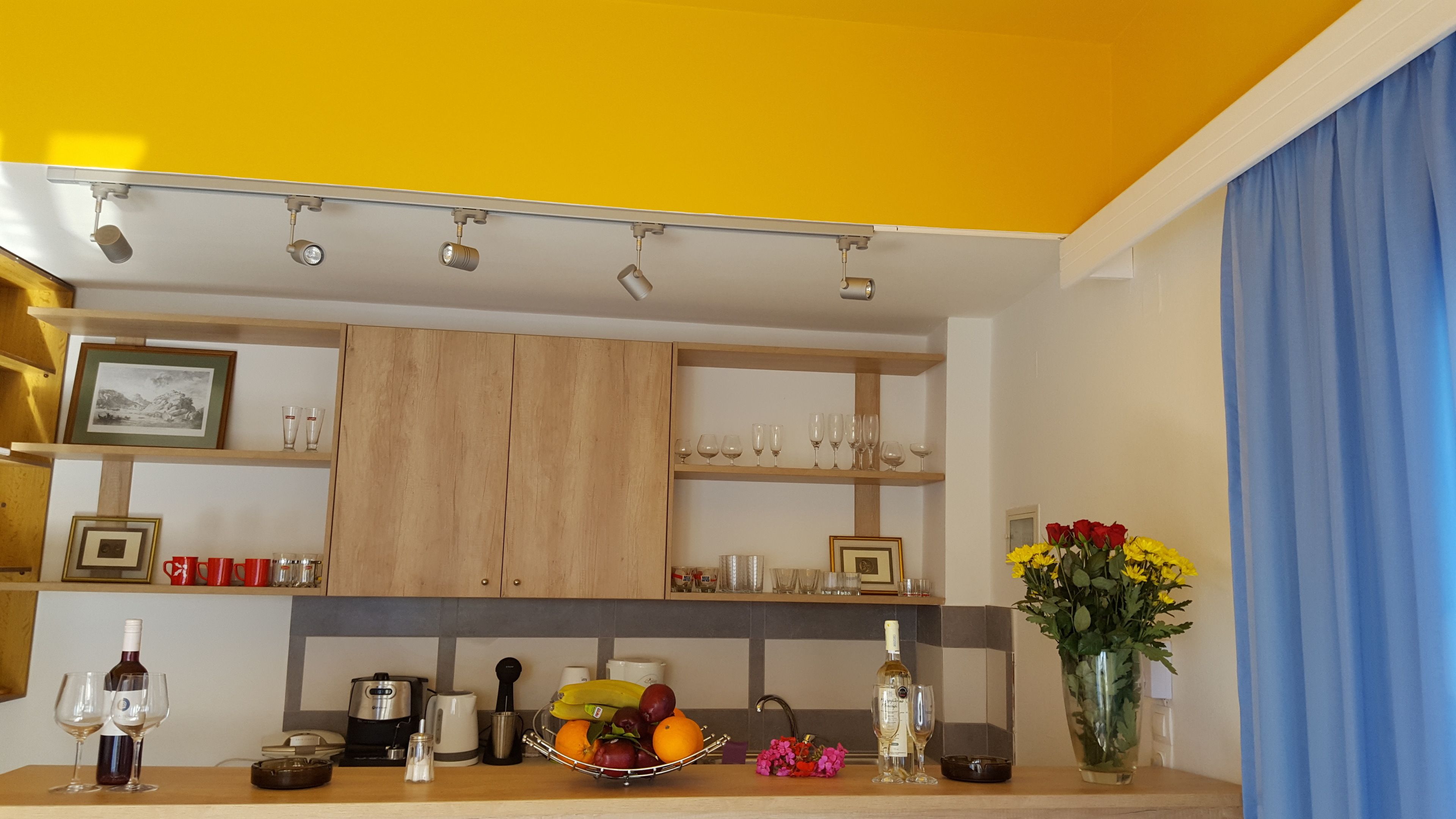 A kitchen with wooden cabinets, a countertop with wine glasses, a fruit bowl, and a vase with flowers.