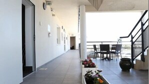 A long, narrow corridor with a white planter box filled with flowers, leading to a balcony area with a table and chairs. - Hôtel Restaurant les Pielettes (Le Rove)