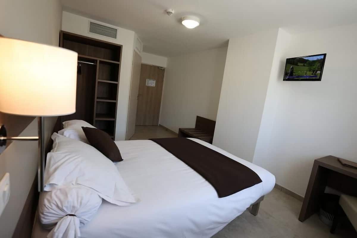 Quarto de hotel com cama, escrivaninha, televisão e guarda-roupa.