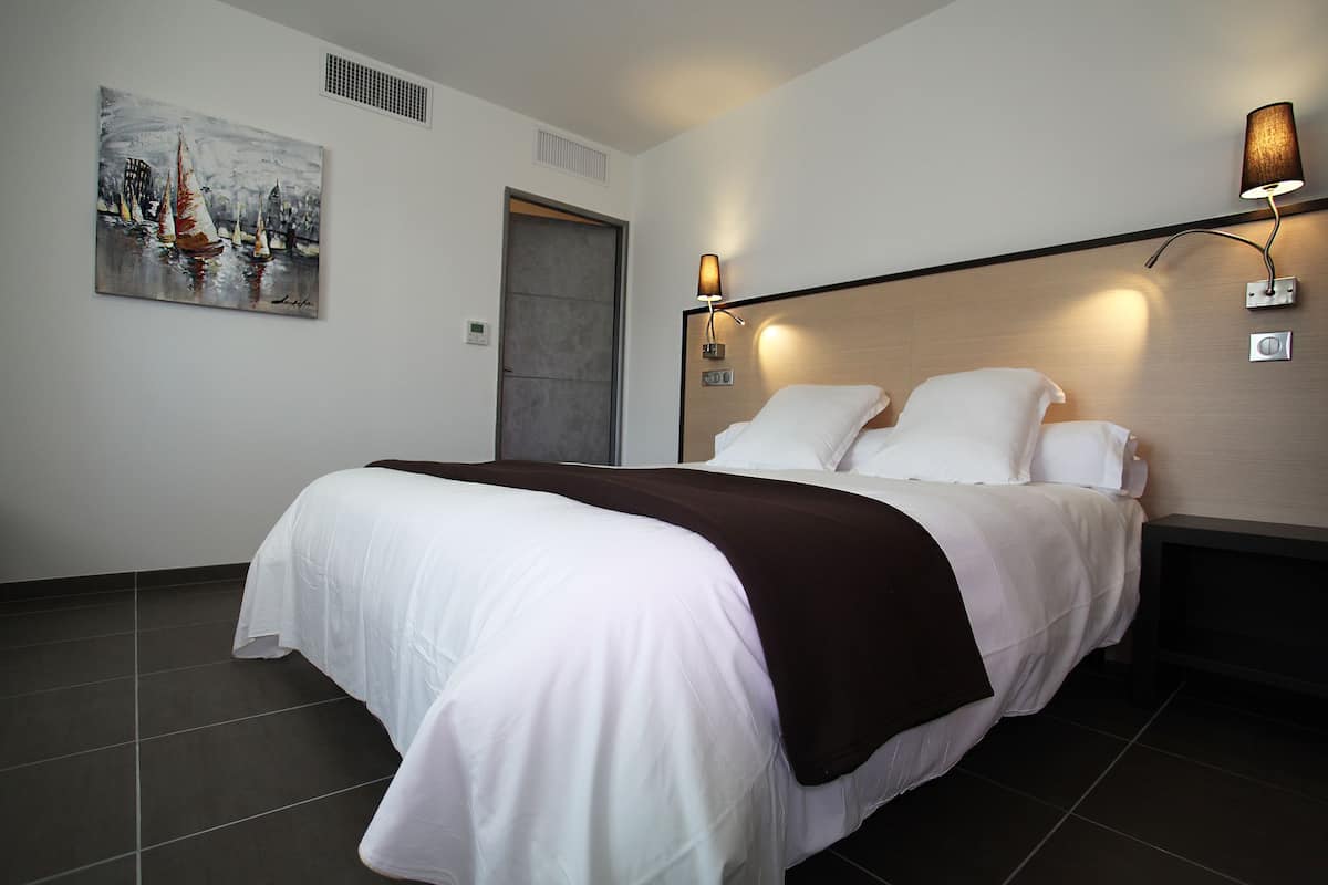 Quarto de hotel com uma cama grande, um quadro na parede e duas luminárias de parede.