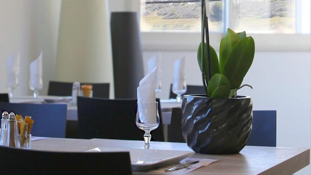 A dining table with a vase of white orchids, a candle, and a menu. - Hôtel Restaurant les Pielettes (Le Rove)