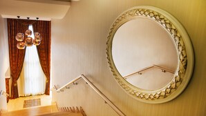 A staircase with a handrail, a round mirror with a decorative frame, and a window with curtains. - Cukurova Erten Otel (Adana)