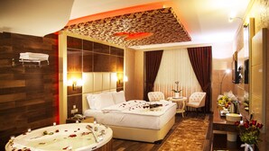 A hotel room with a large bed, a separate sitting area, a bathtub with rose petals, and a breakfast tray on the side. - Cukurova Erten Otel (Adana)