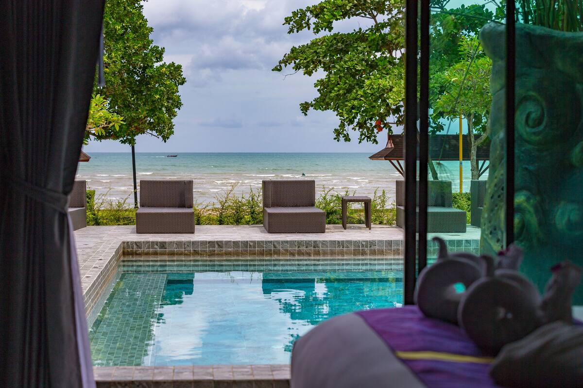 A pool with clear water, surrounded by wicker furniture and a view of the ocean.
