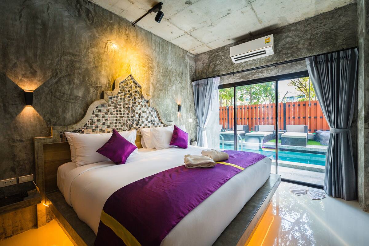 A modern hotel room with a large bed, a view of a swimming pool, and a concrete wall design.