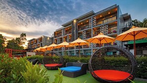 Een hotel met buiten zitplaatsen, waaronder rieten stoelen en tafels, en een gebouw met balkons.