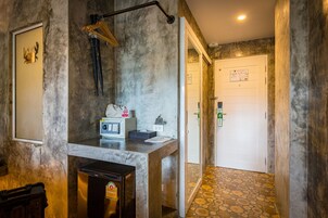 Een badkamer met een handdoekhouder, een klein wastafeltje, een spiegel, een koelkast en een deur met een bordje.
