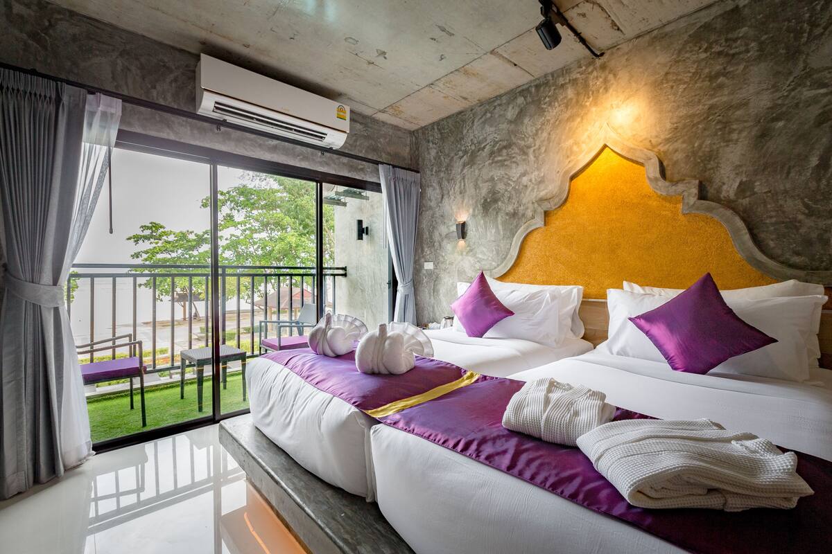 A hotel room with two beds, a balcony with a view, and an air conditioning unit.