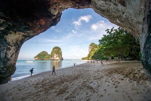 A beach with a natural rock arch, clear blue water, and distant rocky formations. - Maneetel Krabi Beachfront (Krabi)