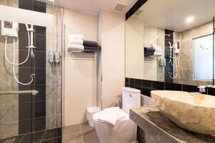 Un baño moderno con ducha de vidrio, inodoro blanco y un lavamanos de piedra grande.