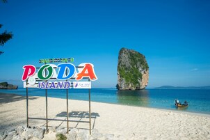 Een strandbordes voor Poda Island, met een helder uitzicht op de oceaan en een grote rotsformatie op de achtergrond.