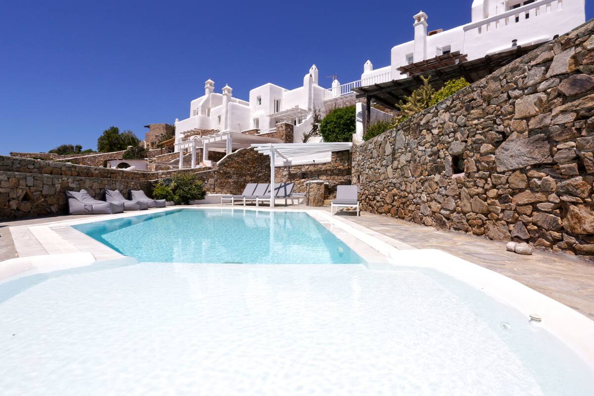Una piscina con sillones blancos y una pared de piedra.