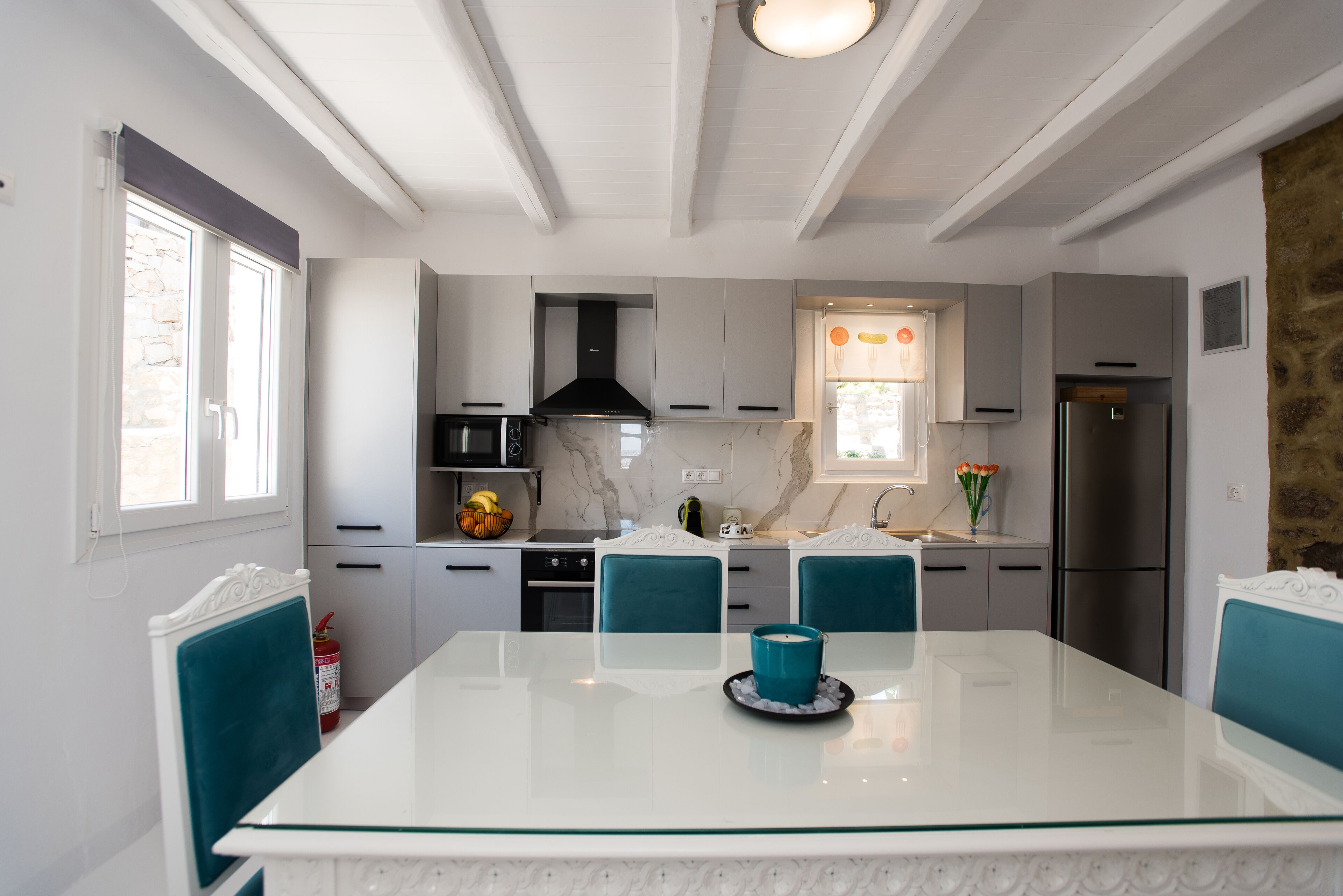 A modern kitchen with white cabinetry, a marble countertop, and a dining table with teal chairs.