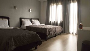 Habitación de hotel con dos camas, un ventanal con cortinas, una mesita con una botella y un cesto de basura.