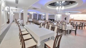 Un comedor amplio con mesas y sillas largas, candelabros elegantes y un diseño de techo moderno.