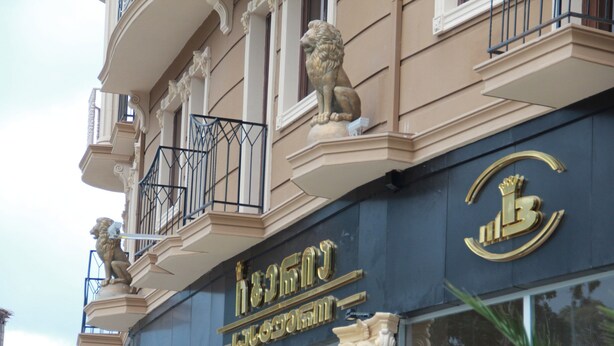 Fachada de edificio con balcones ornamentales, estatuas de leones y un emblema dorado destacado.