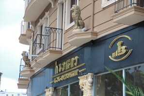 Fachada de edificio con balcones ornamentales, estatuas de leones y un emblema dorado destacado.
