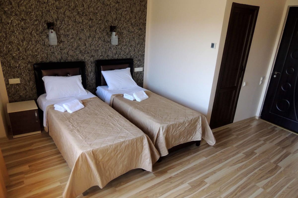 A hotel room with two single beds, wooden flooring, a dark door, and a textured wall.