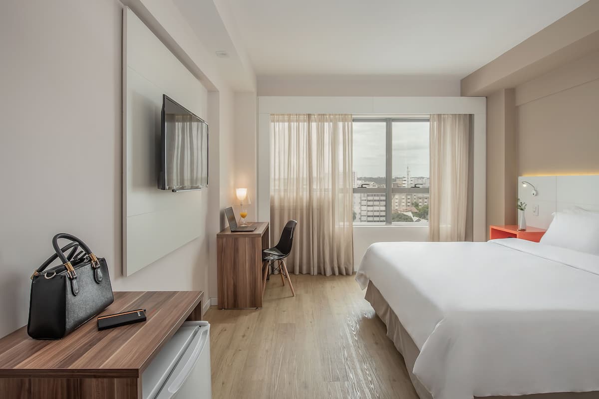 Een hotelkamer met een bed, bureau, stoel, televisie en uitzicht over de stad.