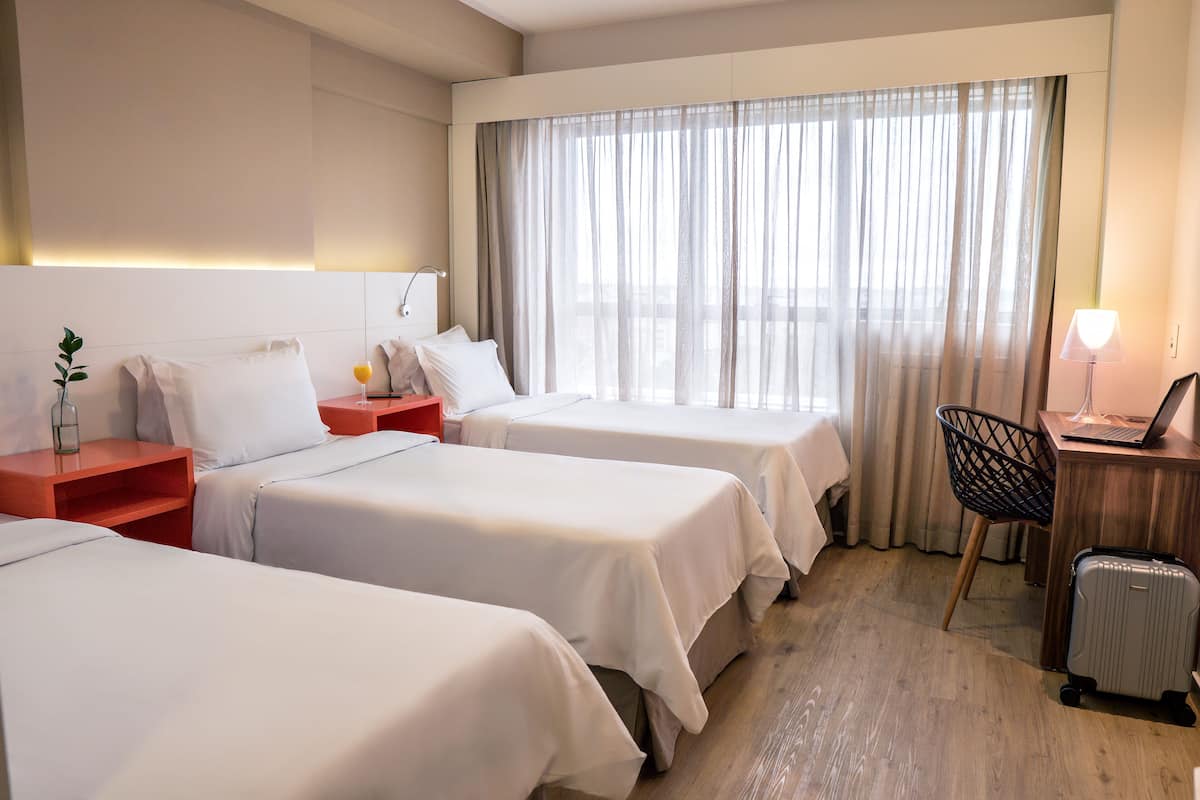 Een hotelkamer met twee bedden, een bureau met een laptop, een stoel en een koffer.