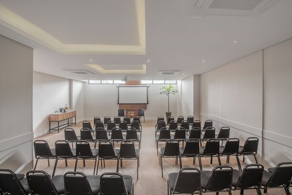 Un salón de conferencias con filas de sillas, un atril y una pantalla de proyector.