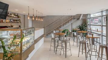 Um café moderno com uma vitrine de doces, banquetas de metal e uma escada que leva a um andar superior.