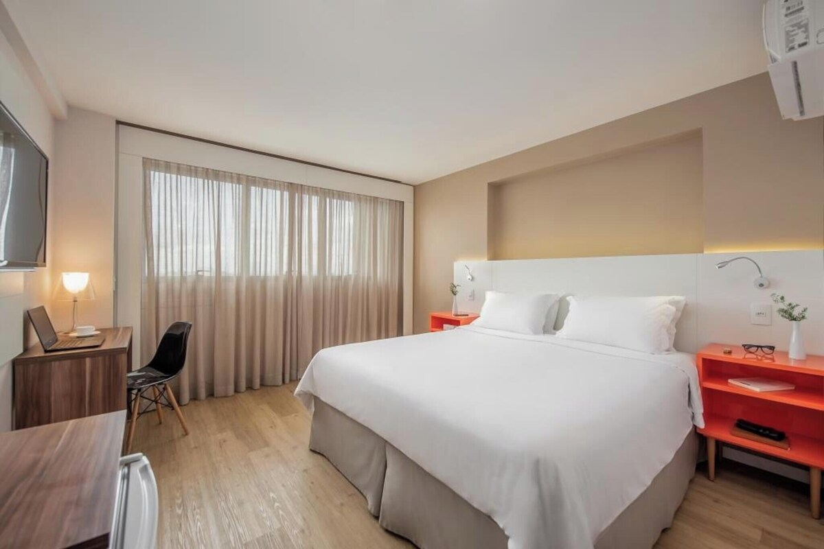 Una habitación de hotel con una cama grande, un escritorio con una silla, un televisor y una ventana con cortinas.