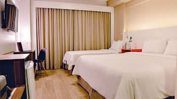 Quarto de hotel com duas camas, uma escrivaninha, uma cadeira, televisão e uma janela grande com cortinas.