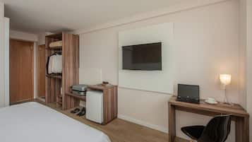 Habitación de hotel con cama, escritorio con computadora portátil, televisión, armario y un refrigerador pequeño.
