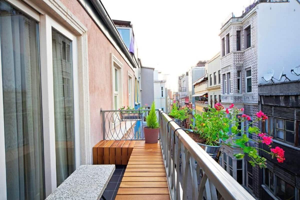 A narrow balcony with wooden flooring, a potted plant, and flowering plants.